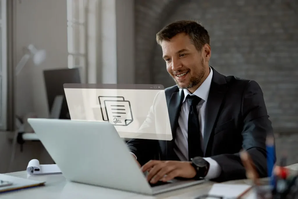 Homem de terno sentado a uma mesa de escritório com um laptop.