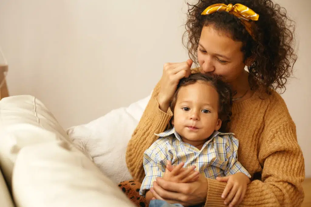 Mãe segurando bebê no colo, sentada em um sofá, com o rosto sobre sua cabeça