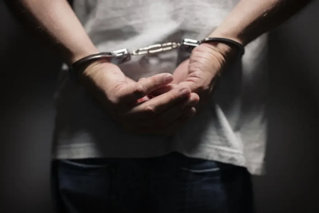 Homem de camiseta branca com as mãos algemadas nas costas